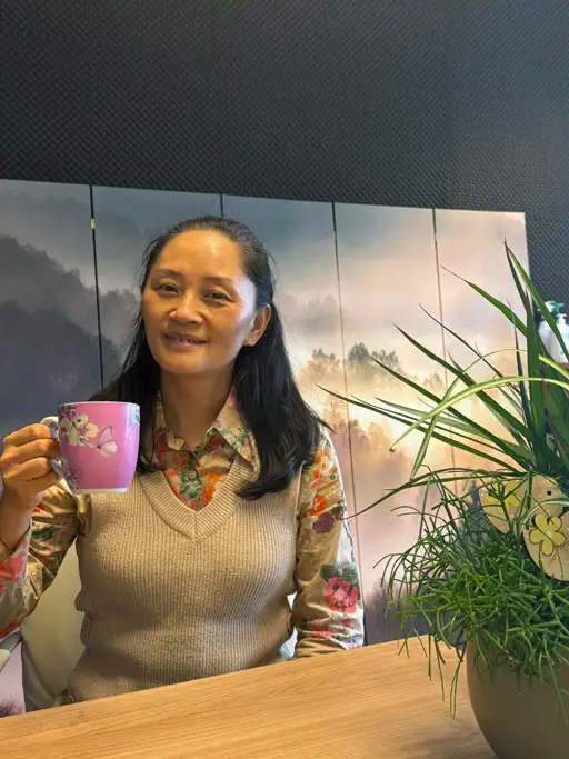 Emilia Chen, hypnotherapeut bij Quick Reset in Alkmaar, zittend met een roze mok in de praktijk.
